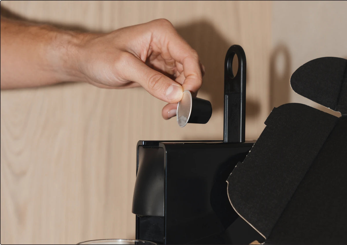 A hand dropping a Coffydoor pod into a Nespresso Original machine