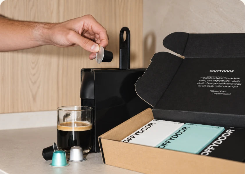 A hand loading a Coffydoor pod into a machine beside an open delivery box