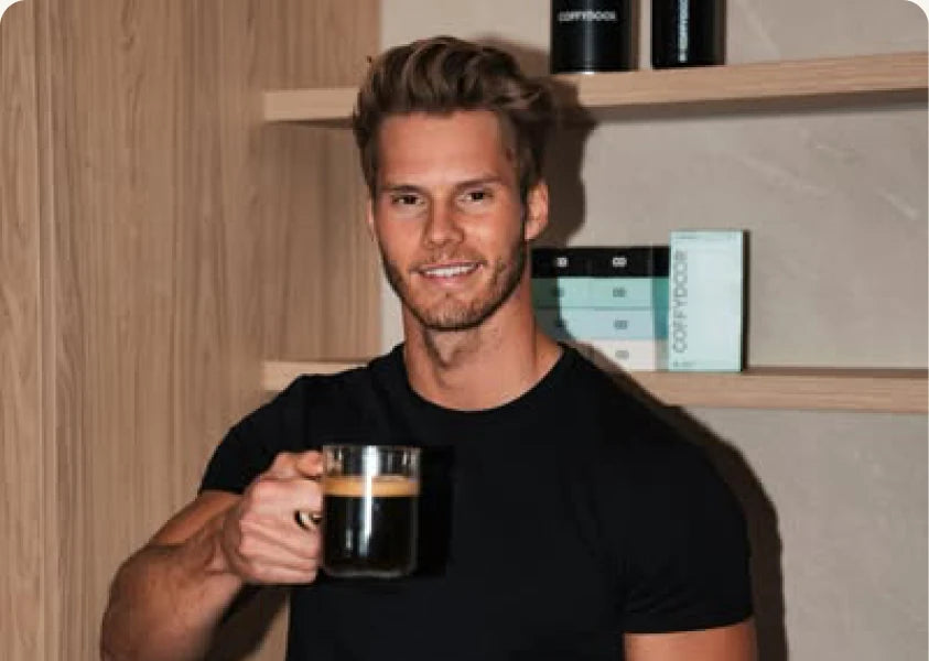 Coffydoor co-founder holding a glass of coffee in front of a shelf of stock