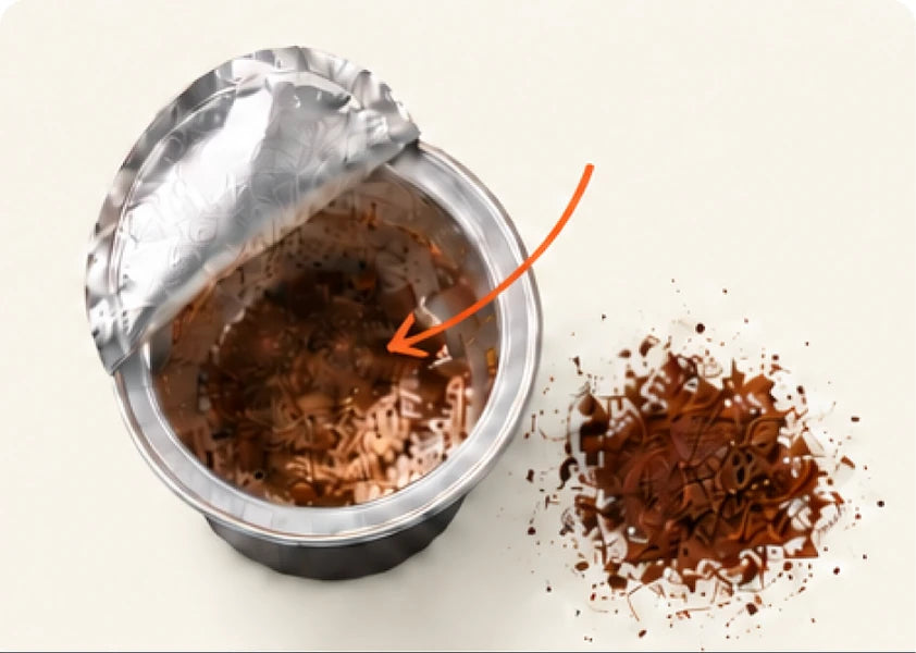 An opened coffee pod beside a small pile of ground coffee.